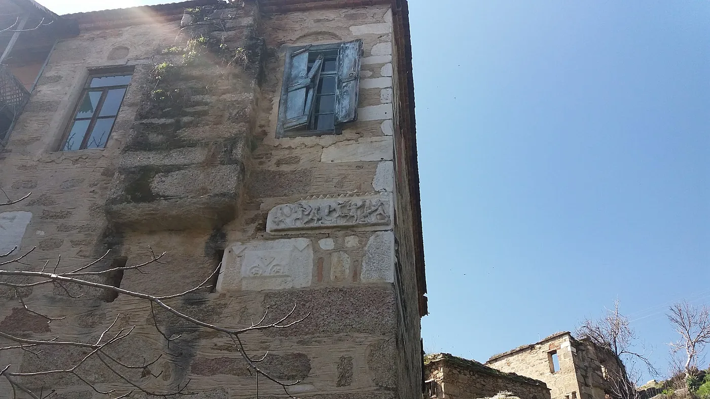 Devşirme antik taşlarla örülmüş eski bir taş evin cephesi; ahşap kepenkler ve kabartmalı mermer bloklar